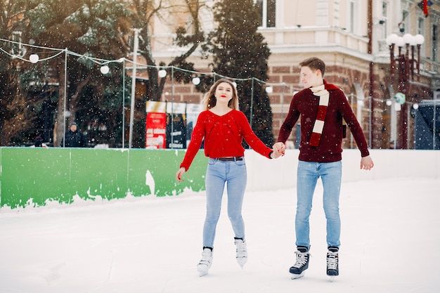 Linda pareja en un suéter rojo divirtiéndose en una arena de hielo