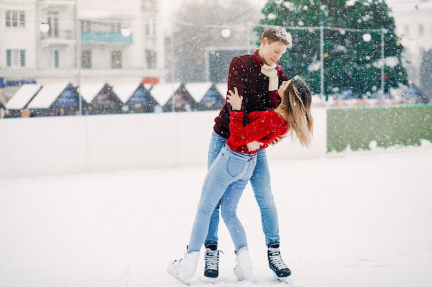 Linda pareja en un suéter rojo divirtiéndose en una arena de hielo