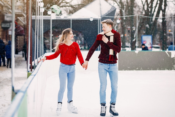 Foto gratuito linda pareja en un suéter rojo divirtiéndose en una arena de hielo