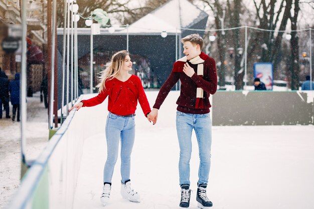 Linda pareja en un suéter rojo divirtiéndose en una arena de hielo