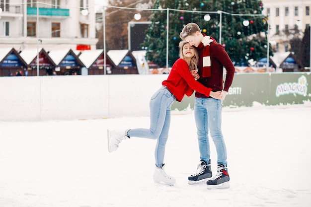 Linda pareja en un suéter rojo divirtiéndose en una arena de hielo