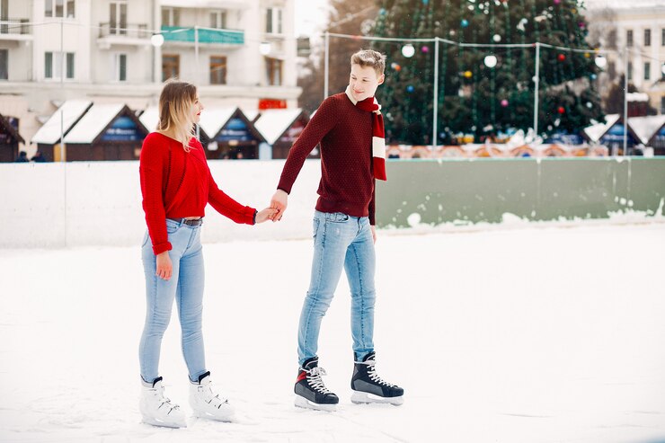 Foto gratuito linda pareja en un suéter rojo divirtiéndose en una arena de hielo