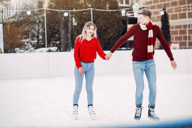 Linda pareja en un suéter rojo divirtiéndose en una arena de hielo