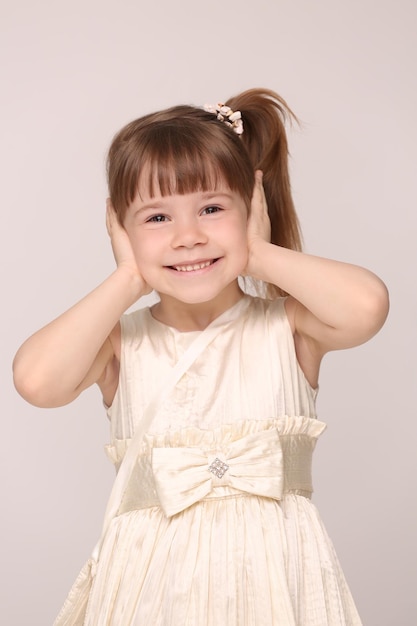 La linda y pequeña dama de la momia cerró los oídos. Chica en vestido blanco con cola de caballo sonriendo.