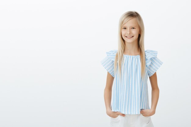 Linda señorita de compras con mamá. Feliz niña feliz en blusa azul, tomados de la mano en las caderas y sonriendo ampliamente, asombrado, divirtiéndose con amigos sobre pared gris