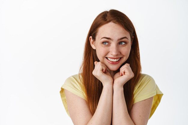 Linda y tonta chica pelirroja, sonriendo y luciendo romántica a un lado del logo, apoyada en las manos y soñando despierta, pensando en algo nostálgico, de fondo blanco.