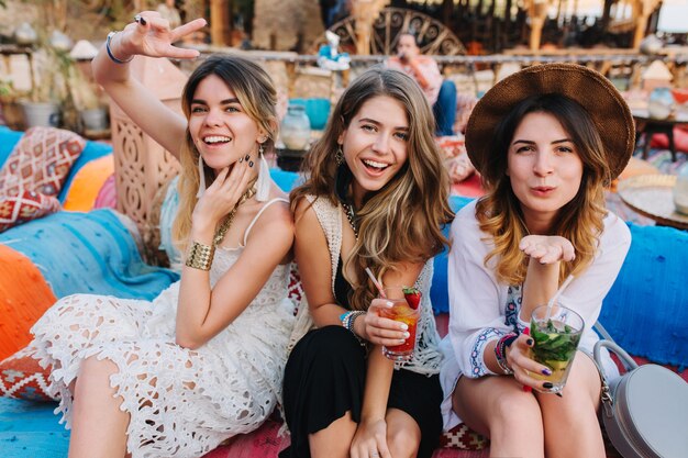 Lindas hermanas sonrientes que pasan tiempo en un restaurante al aire libre, posando con signos de beso de paz y aire