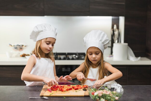 Lindas hermanitas cortando pimiento en tabla de cortar mientras preparan comida