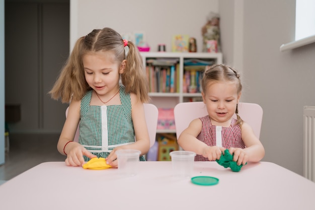 Lindas niñas moldeadas de plastilina en mesa rosa