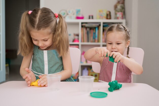 Lindas niñas moldeadas de plastilina en mesa rosa