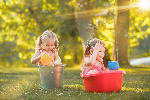 Las lindas niñas rubias jugando con salpicaduras de agua en el campo en verano