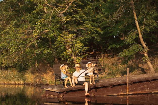Lindas niñas y su abuelo están pescando en el lago o río