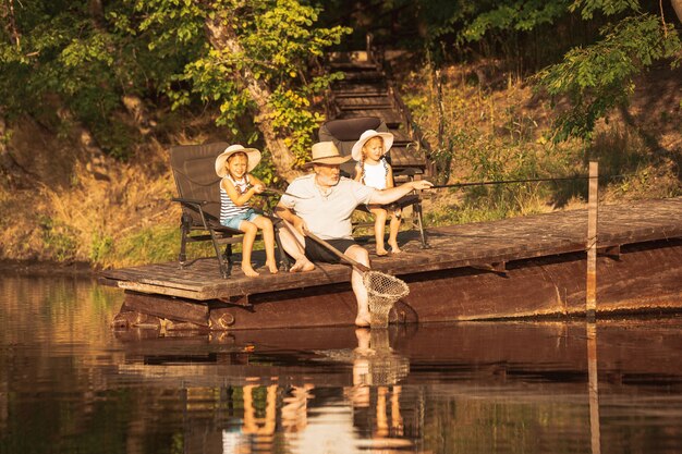 Lindas niñas y su abuelo están pescando en el lago o río