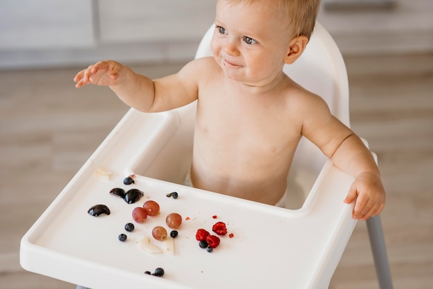 Foto gratuita lindo bebé de ángulo alto en silla alta eligiendo qué fruta comer