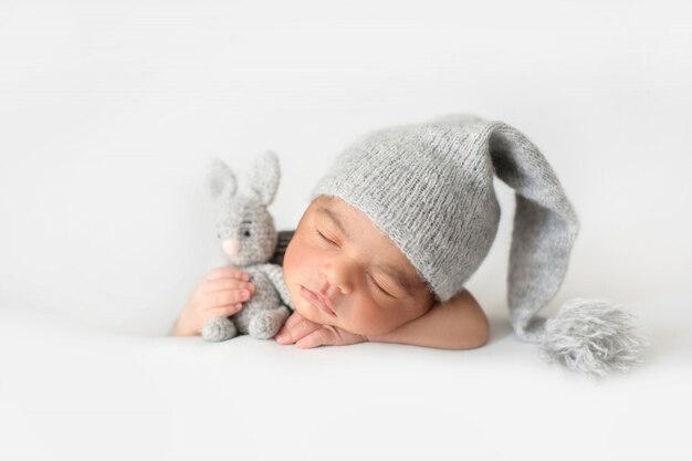 Lindo bebé durmiendo con gorro de ganchillo gris y con conejo de juguete