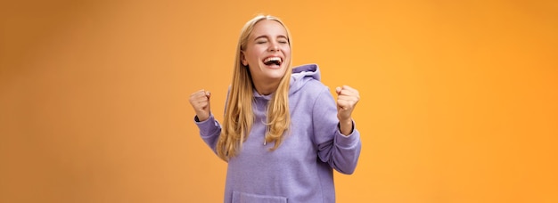 Foto gratuita lindo feliz triunfante chica europea rubia con capucha gritando sí lograr el sueño de toda la vida apretado