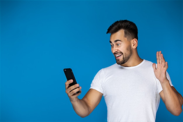 Lindo hombre europeo sonríe al teléfono y agita su mano