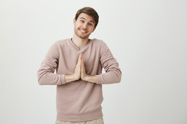 Lindo hombre tonto sonriendo suplicando, tomados de la mano en oración, suplicando o diciendo por favor