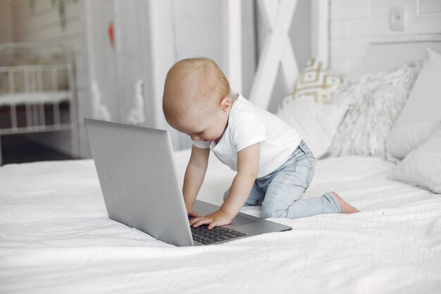 Lindo niño jugando con una computadora portátil en una cama