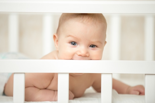 Lindo niño mirando interesado a través del marco de la cuna del bebé