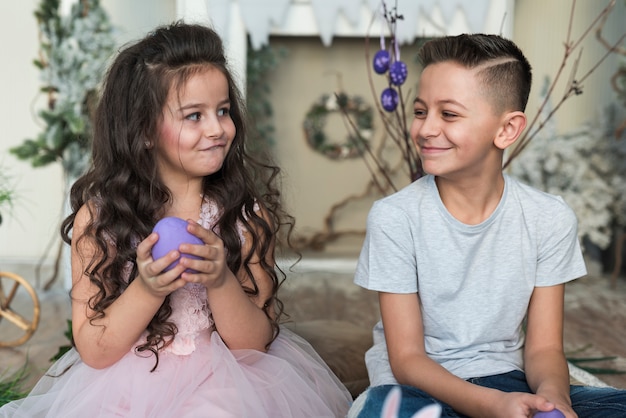 Lindo niño y niña sentada con huevos de Pascua