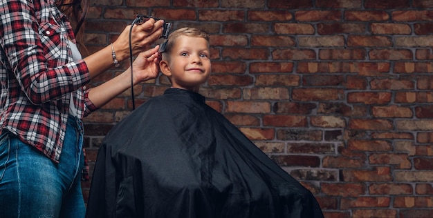 Lindo niño preescolar cortándose el pelo. El peluquero infantil con cortapelos está cortando a un niño pequeño en la habitación con interior de loft.