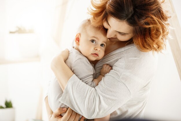 El lindo niño recién nacido mira a un lado con miedo, mientras que la atractiva joven madre abraza suavemente al bebé expresando su amor y apoyo. Concepto de familia