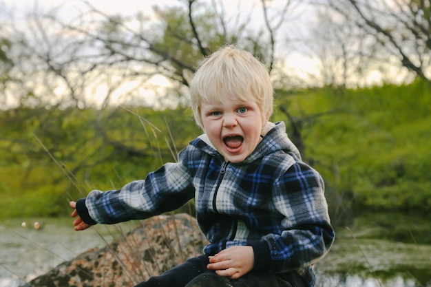 Lindo niño rubio sentado en una roca en un parque