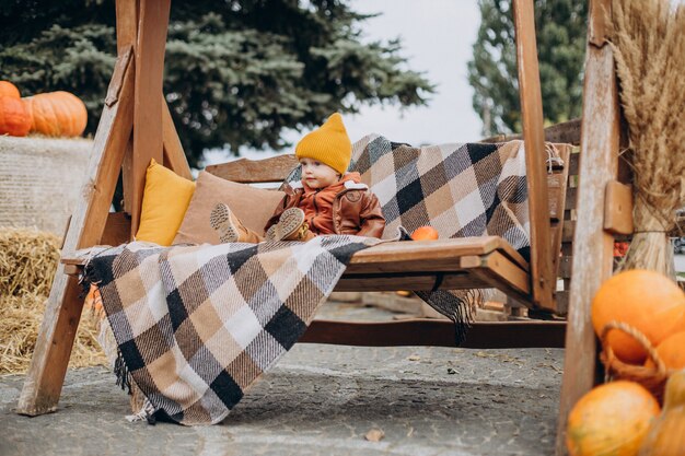 Lindo niño sentado en un columpio con calabazas de halloween en el rancho