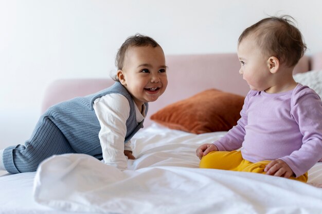 Lindos bebés jugando entre ellos en la cama y sonriendo