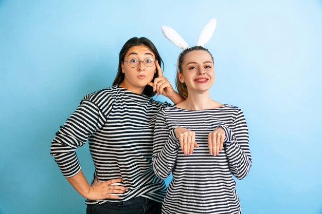 Lindos conejitos. Mujeres emocionales jóvenes aisladas sobre fondo azul degradado de estudio. Concepto de emociones humanas, expresión facial, amistad, anuncio. Hermosas modelos femeninas caucásicas en ropa casual.