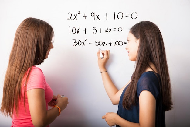 Foto gratuita lindos jóvenes estudiantes de secundaria resolviendo algunas ecuaciones de álgebra en una pizarra blanca