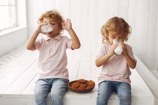 Lindos niños comiendo galletas y bebiendo leche