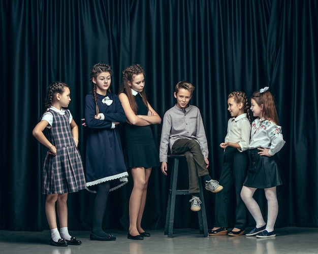 Lindos niños con estilo sobre fondo oscuro de estudio. Las hermosas adolescentes y el niño parados juntos