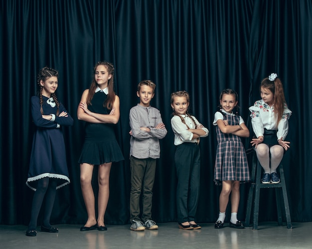 Lindos niños con estilo sobre fondo oscuro de estudio. Las hermosas adolescentes y el niño parados juntos