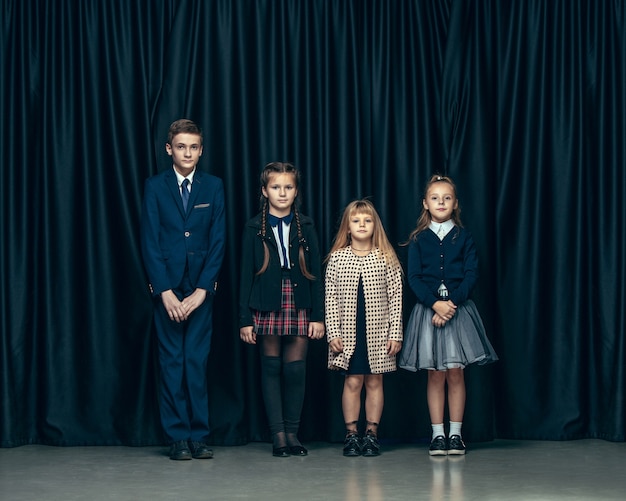 Lindos niños con estilo sobre fondo oscuro de estudio. Las hermosas adolescentes y el niño parados juntos