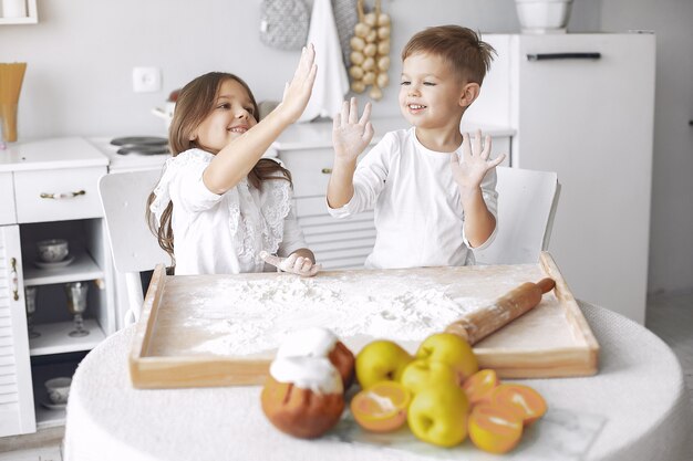 Lindos niños pequeños sentados en una cocina con masa