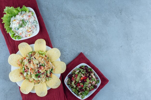 Línea de ensaladas variadas adornadas con hojas de lechuga y patatas fritas sobre mármol.