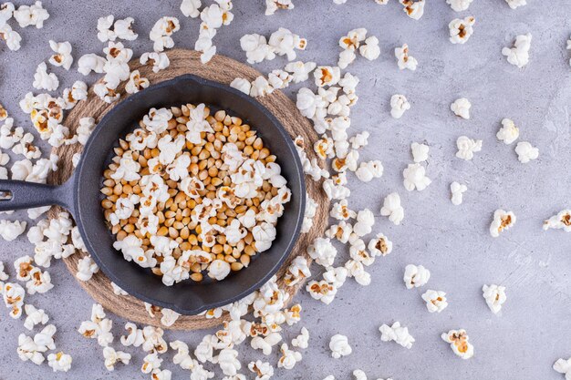 Lío de palomitas de maíz esparcidas con una sartén llena de grano en el medio sobre fondo de mármol. Foto de alta calidad