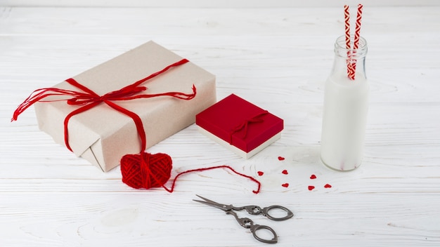 Líquido blanco en botella con tubos cerca de pequeños corazones, tijeras y regalos.