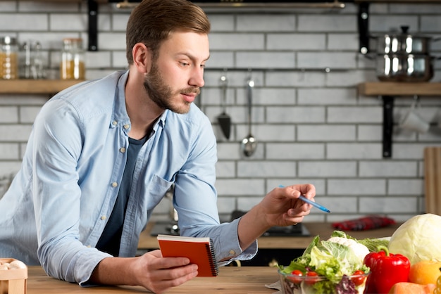 Lista de compras de la escritura del hombre joven en cocina