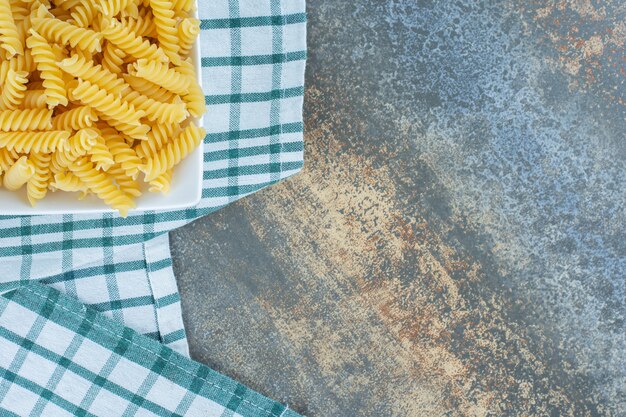 Listo para cocinar la pasta fusilli en un bol sobre una toalla, sobre la superficie de mármol.