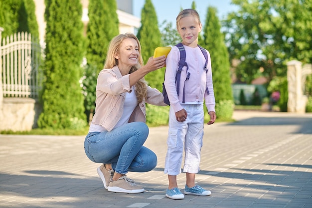 Listo para la escuela. Mamá arreglando una mochila en la espalda de sus hijos