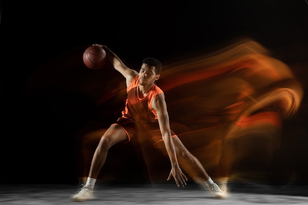 Listo. joven jugador de baloncesto árabe musculoso en acción, movimiento aislado en negro en luz mixta