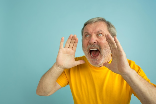 Llamando, gritando. Retrato de hombre caucásico aislado sobre fondo azul de estudio. Hermoso modelo masculino en camisa amarilla posando.