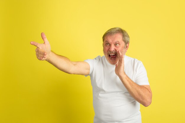 Llamando, señalando. Retrato de hombre caucásico aislado sobre fondo amarillo de estudio. Hermoso modelo masculino en camisa blanca posando. Concepto de emociones humanas, expresión facial, ventas, publicidad. Copyspace.