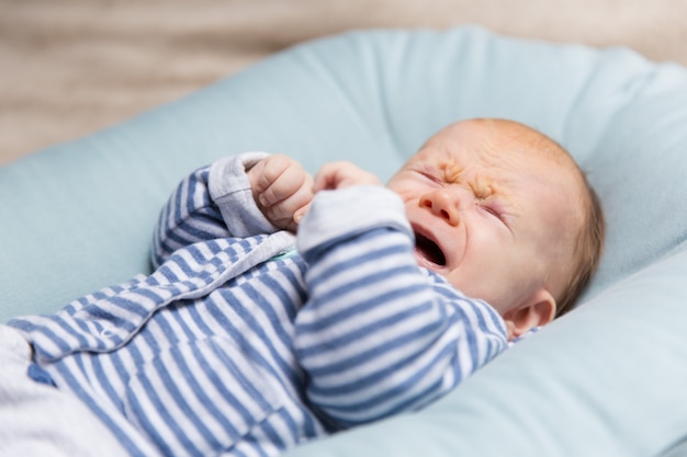 Llorando bebé pelirrojo con ropa azul y gris