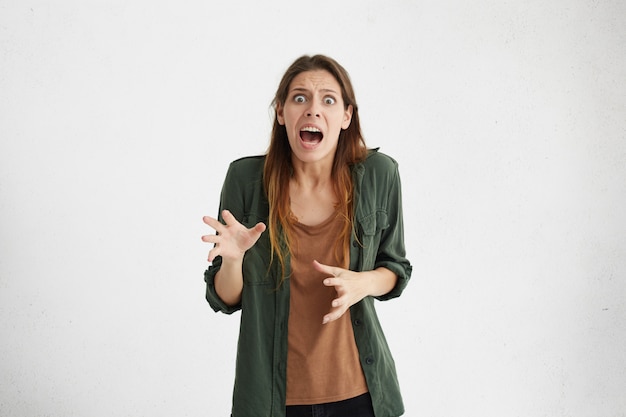 Loca y desesperada mujer sorprendida mirando con la boca abierta y los ojos saltones gritando de horror.