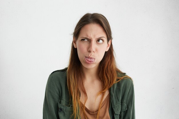 Loca mujer atractiva que muestra sus ojos con el ceño fruncido lengua mirando a un lado con alegría.