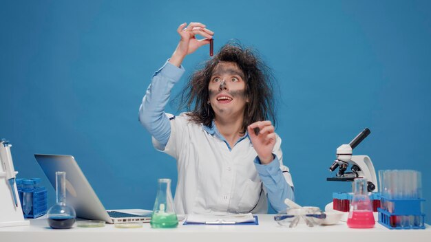 Loca y tonta química femenina trabajando con microscopio en el estudio, actuando loca y loca en cámara. Una mujer divertida y tonta que se siente tonta y es divertida, una científica loca y juguetona con el pelo desordenado.